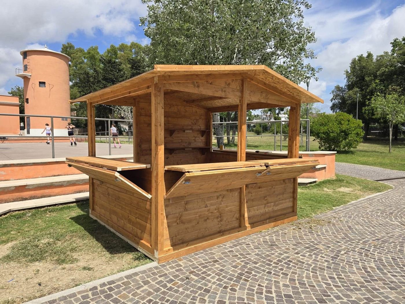 Chiosco in legno naturale con aperture a bancone su tre lati, installato su pavimentazione esterna